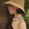 HAT ADIGE 2 Side profile of a woman wearing the ADIGE handwoven natural straw hat outdoors beside a tree.