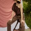 HAT ADIGE 3 Woman sitting outdoors wearing the ADIGE handmade straw sun hat and brown linen outfit.
