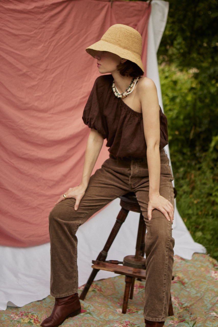 HAT ADIGE 3 Woman sitting outdoors wearing the ADIGE handmade straw sun hat and brown linen outfit.