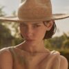 Close-up portrait of a woman wearing the PIAVE handwoven straw fedora hat with a natural golden finish.