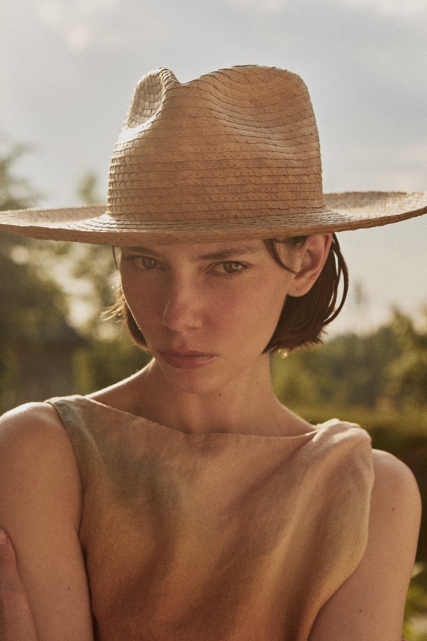 Close-up portrait of a woman wearing the PIAVE handwoven straw fedora hat with a natural golden finish.