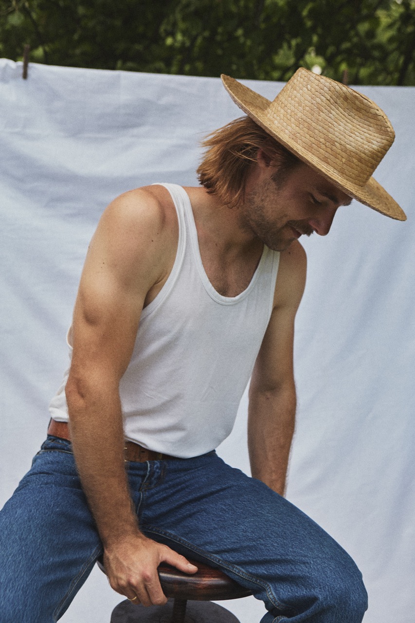 Man seated outdoors wearing the PIAVE II handwoven straw fedora hat in a relaxed summer setting.