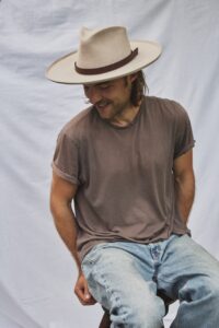 Man seated wearing the PIAVE handwoven straw fedora hat with a classic summer silhouette.