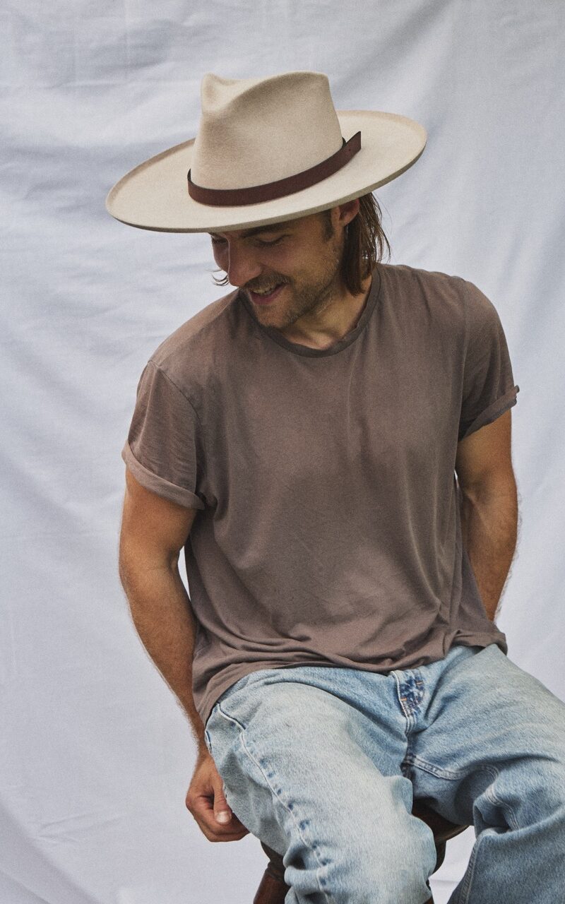 Man seated wearing the PIAVE handwoven straw fedora hat with a classic summer silhouette.