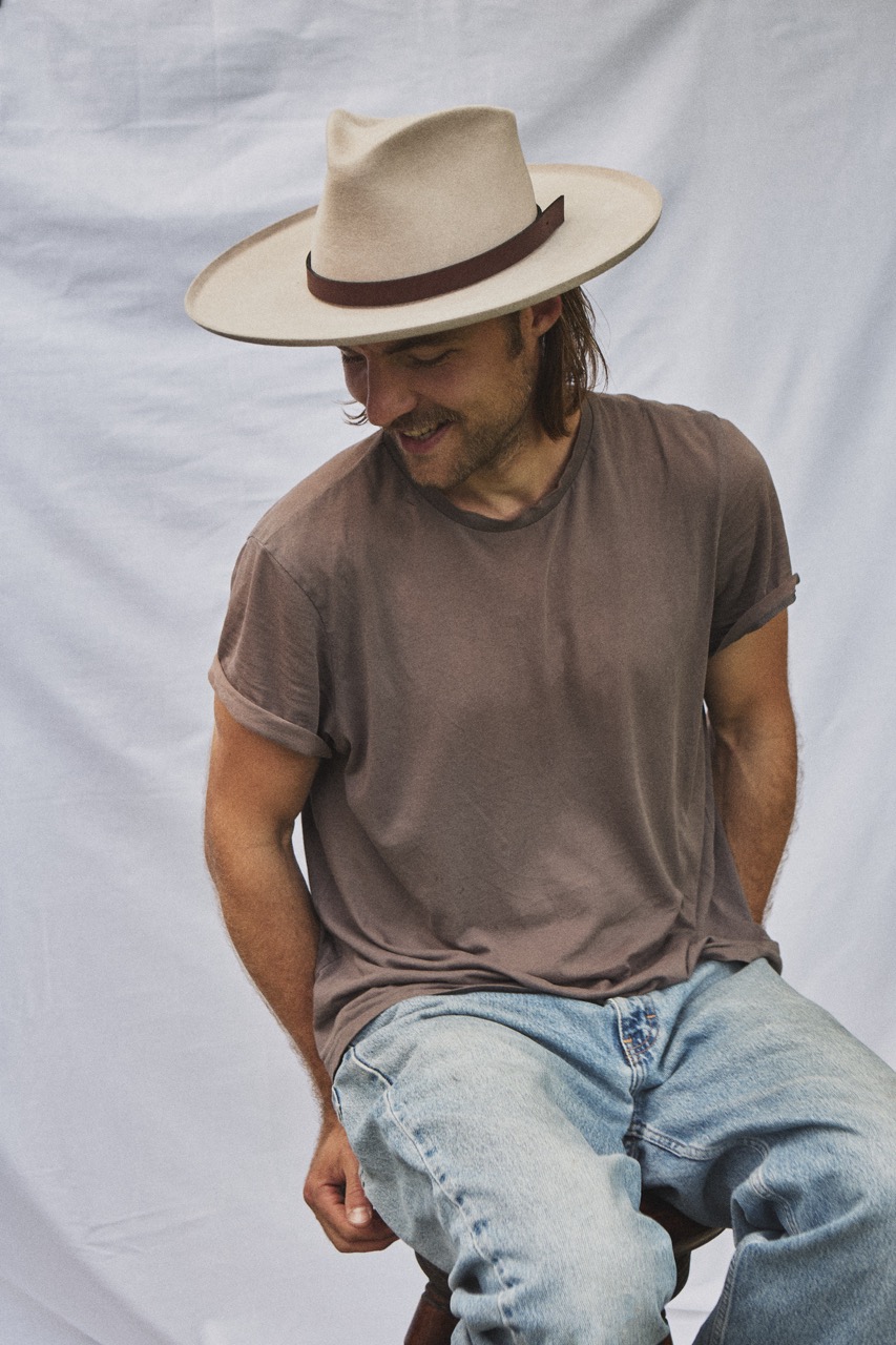 Man seated wearing the PIAVE handwoven straw fedora hat with a classic summer silhouette.